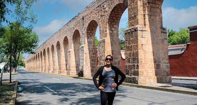 Woman posing on an empty street beside the historic stone aqueduct of Morelia.