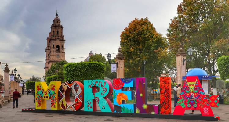 Colorful 3-D letters spelling MORELIA with a historic cathedral tower rising behind them.