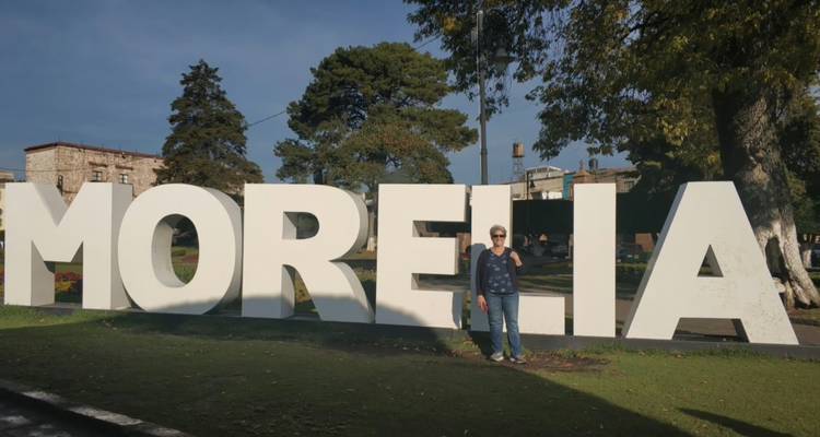 Visitor standing beside large white block letters spelling MORELIA on a grassy park lawn.