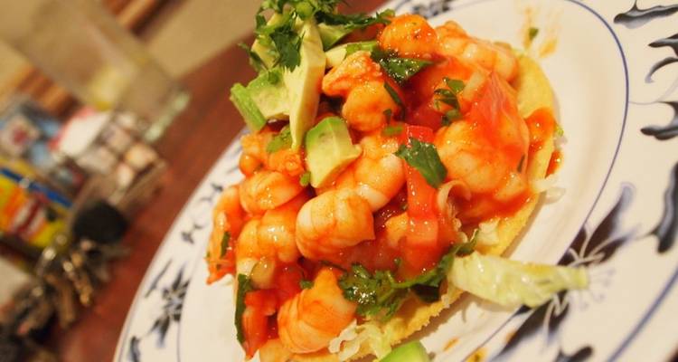 Nahaufnahme einer Garnelen-Tostada mit Avocado und Koriander auf einem gemusterten Teller.