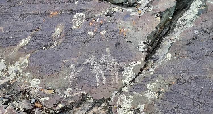 Uralte Petroglyphen von menschlichen Figuren, die in zerklüfteten lila-grauen Fels geätzt sind.