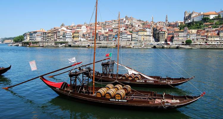 Traditionele rabelo-boten geladen met wijnvaten voor anker op de Douro-rivier tegenover de skyline van Porto