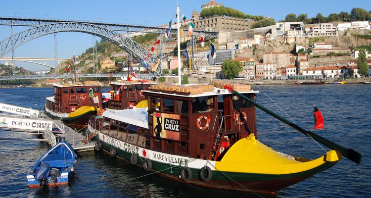 Kleurrijke riviercruiseboten afgemeerd met Porto's Dom Luís I brug en heuvelbebouwing op de achtergrond