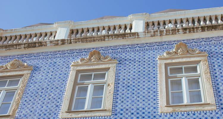 Gevel bedekt met traditionele blauwe azulejo tegels met sierlijke ramen tegen een heldere hemel