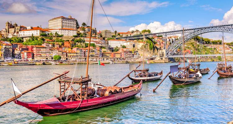 Bateaux rabelo traditionnels amarrés sur le fleuve Douro avec l'horizon coloré de Porto et le pont en fer.