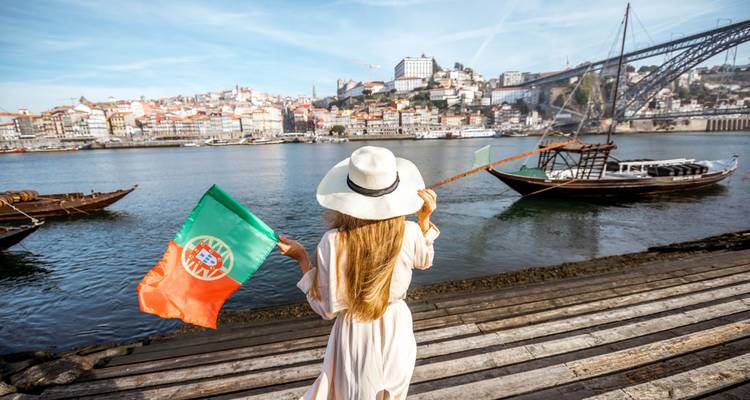 Une femme agite un drapeau portugais sur la rive du Douro avec l'horizon de Porto en arrière-plan.