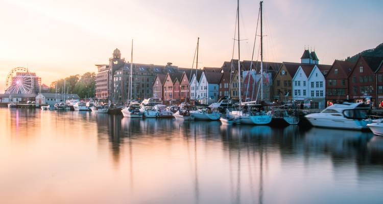 Das weiches goldenes Licht der Goldenen Stunde spiegelt sich auf dem ruhigen Hafenwasser von Bergens Bryggen mit Booten und Holzhäusern wider.