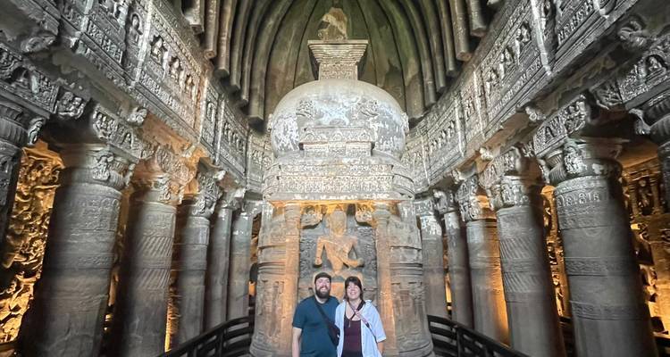 Gran interior de una sala chaitya con columnas ornamentadas y estupa, con dos visitantes en la base para dar escala.