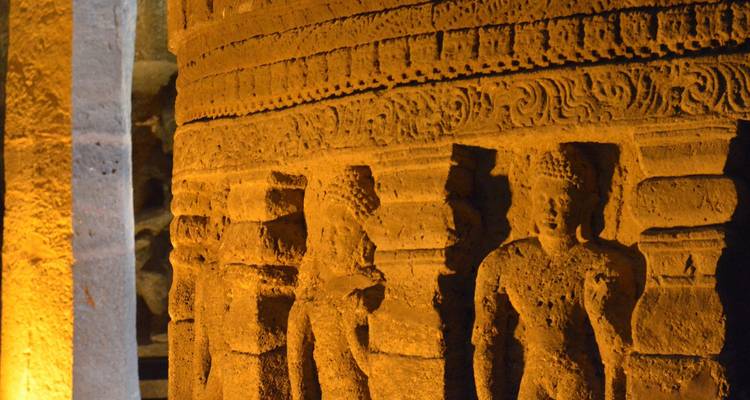 Primer plano cálidamente iluminado de pilar de piedra cilíndrico intrincadamente tallado con figuras humanas.