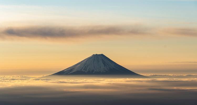 Der Fuji, der bei Sonnenaufgang über einer weichen Decke aus goldenen Wolken unter pastellfarbenen Himmeln hervorragt.