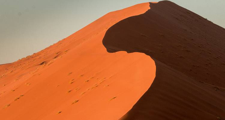 Gesloten abstracte curve van een reusachtige oranje zandduin in zacht avondlicht.
