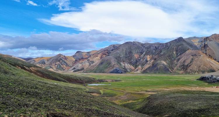 Large vallée verte entourée de crêtes de rhyolite colorées sous un ciel lumineux à Landmannalaugar.