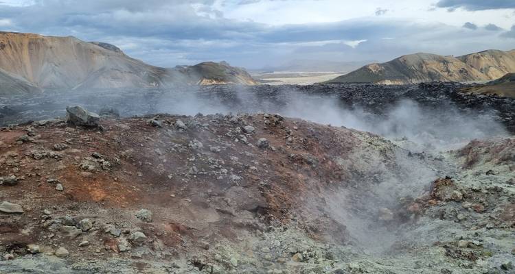 Cratère géothermique fumant libérant de la vapeur au milieu d'un paysage volcanique austère.