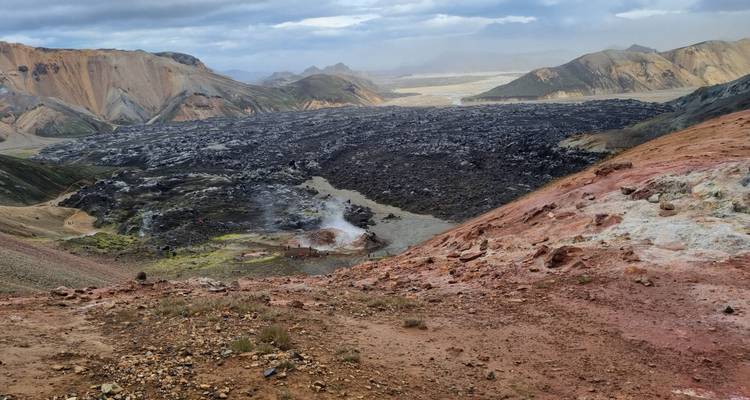 Vue panoramique d'une coulée de lave sombre traversant des collines colorées des hautes terres.