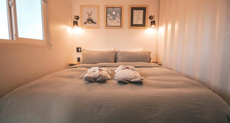 Gemütliches, sanft beleuchtetes Schlafzimmer mit ordentlich gefalteten Bademänteln auf einem großen Bett und gerahmter Kunst an der Wand.