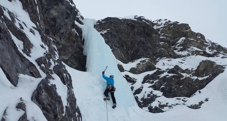 IJsklimmer die een verticale bevroren waterval beklimt op een ruige bergwand.