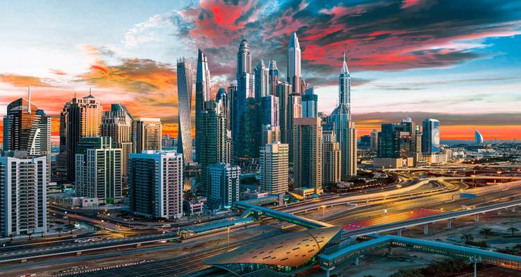 Futuristische Skyline von Dubai bei Sonnenuntergang mit lebendigen Wolken und beleuchteten Autobahnen im Vordergrund.
