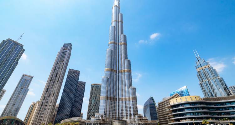 Klare Tagaufnahme des aufragenden Burj Khalifa, umgeben von modernen Wolkenkratzern unter blauem Himmel.