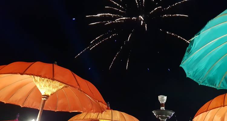 Nachthimmel gefüllt mit Feuerwerk über farbenfrohen Sonnenschirmen bei einem balinesischen Fest.