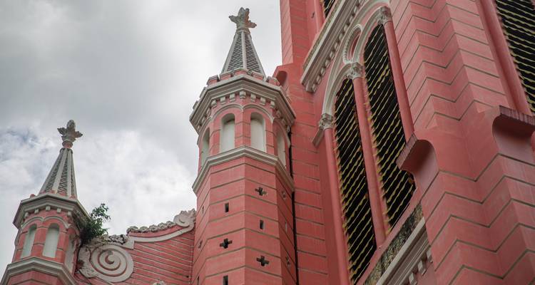 Nahaufnahme einer rosa neogotischen Kirchenfassade mit kunstvollen Türmen, die in den bewölkten Himmel ragen