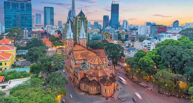 Aerial twilight view of Saigon's Notre-Dame Cathedral amid modern skyscrapers and leafy boulevards.