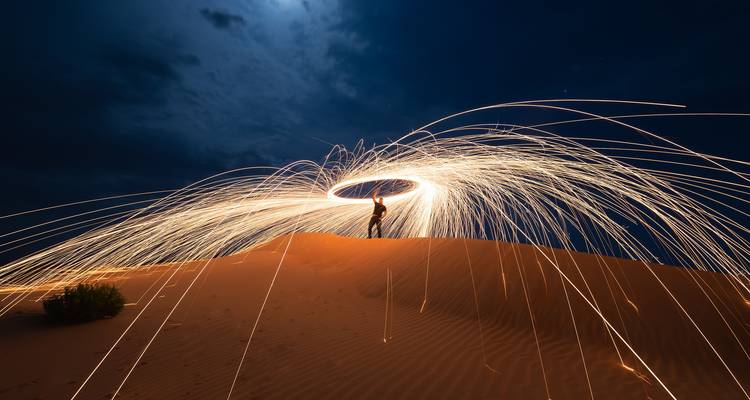 Fotografía de larga exposición nocturna de chispas de lana de acero girando sobre una duna del desierto.