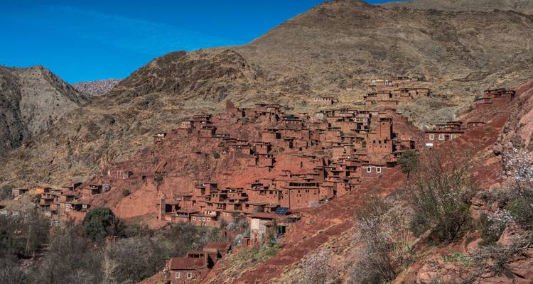 Ansammlung roter Steinhäuser, die sich an einen kargen Atlasgebirgs-Hang unter klarem Himmel klammern