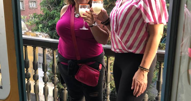 Zwei Frauen genießen Getränke auf einem Balkon, festgehalten als spielerisches Spiegel-Selfie.