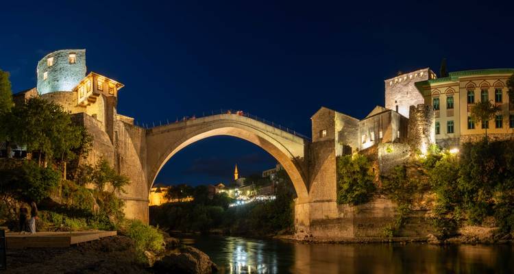 Lange belichtingsnachtfoto van Stari Most verlicht tegen een diepblauwe lucht met reflecties in het water.