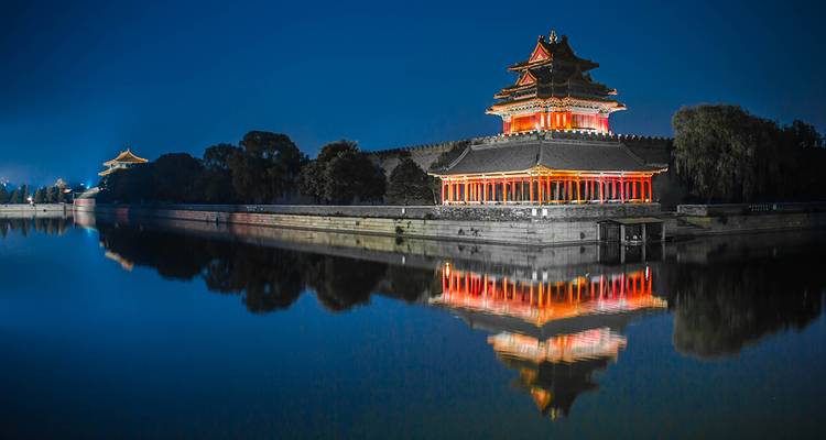Nachtansicht des beleuchteten Eckturms der Verbotenen Stadt in Peking, der sich perfekt im stillen Burggraben spiegelt.