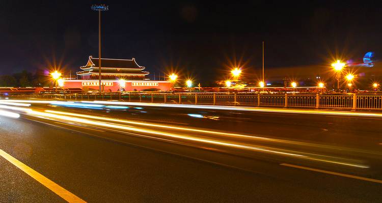 Langzeitbelichtung-Nachtaufnahme des Tiananmen-Tors mit Autolichtspuren, die entlang einer Stadtstraße verlaufen.