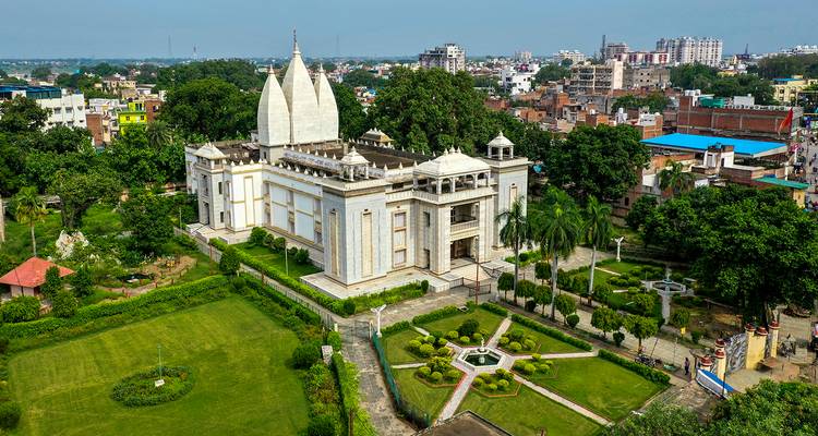 Vue aérienne d'un complexe de temples en marbre blanc entouré de jardins paysagers au sein d'une ville animée.