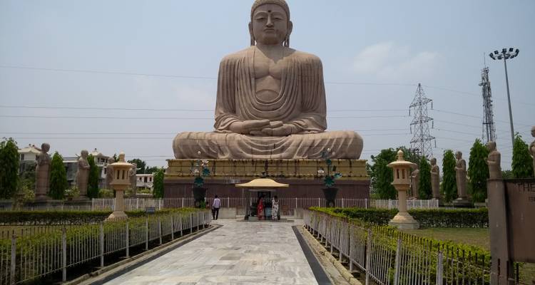 Statue massive de Bouddha en pierre assis à Bodhgaya avec des rangées symétriques de sculptures plus petites le long d'un chemin de marbre.