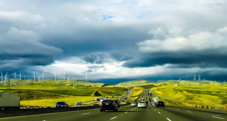 Una autopista muy transitada de varios carriles atraviesa colinas verdes ondulantes salpicadas de aerogeneradores bajo nubes tormentosas.