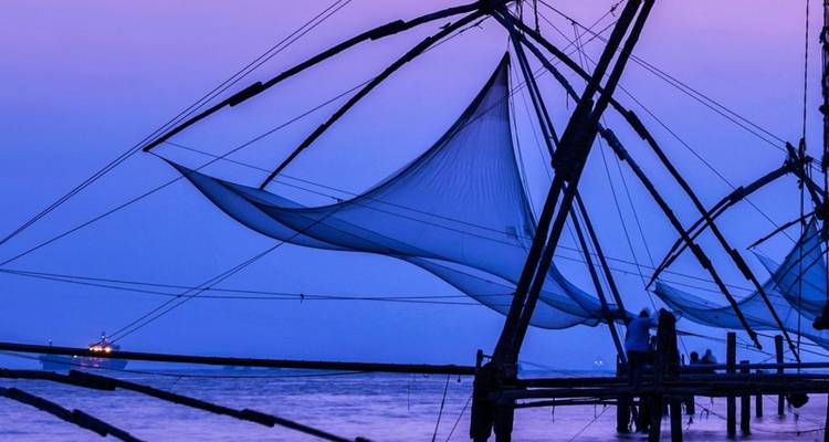 Silhouettierte chinesische Fischernetze erstrecken sich über ruhiges Wasser in der violetten Dämmerung