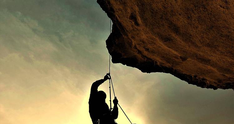 Escalador en silueta asciende una pared de roca vertical al atardecer usando cuerda y arnés