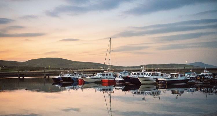 Petits bateaux de pêche amarrés dans un port tranquille au crépuscule avec des cieux pastel reflétés sur l'eau.