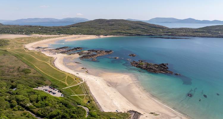 Vue aérienne panoramique d'une plage de sable en croissant et de promontoires émeraude entourés d'une eau turquoise cristalline.