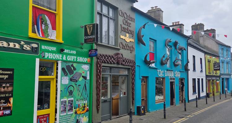 Rue principale animée bordée de façades de magasins aux couleurs vives et de drapeaux irlandais dans une petite ville.