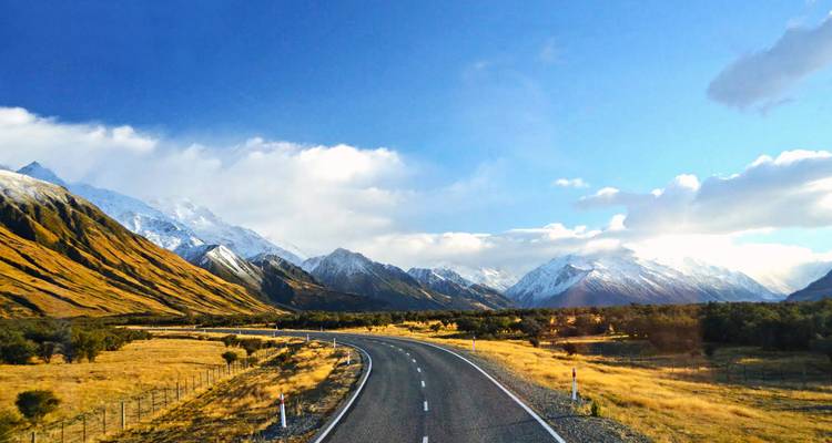 Open highway curves toward snow-capped peaks and wide alpine valley in New Zealand.