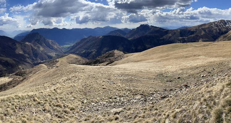 Meseta alpina seca y expansiva con suelo rocoso y crestas distantes bajo nubes fragmentadas