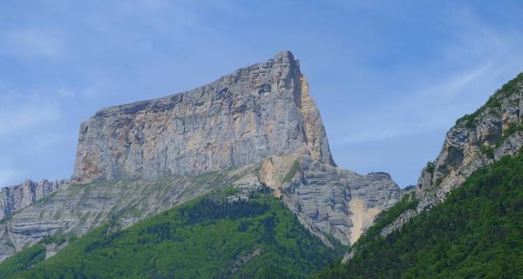 Imponente montaña de paredes verticales que se alza sobre exuberantes laderas verdes contra el cielo azul