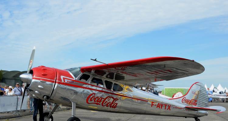 Avión plateado vintage de Coca-Cola en la pista durante un espectáculo aéreo bajo un cielo parcialmente nublado
