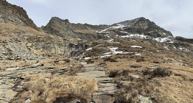Pendiente alpina rocosa con parches dispersos de nieve bajo cielo nublado