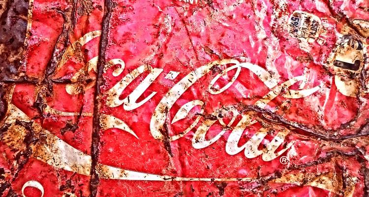 Primer plano de un letrero oxidado y desgastado de Coca-Cola con pintura descascarada