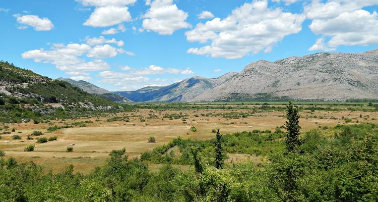 Uitgestrekte landelijke vallei geflankeerd door rotsachtige bergen onder gevlekte wolken