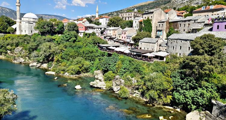 Kleurrijke gebouwen aan de rivier en moskeekoepels weerspiegeld in de turquoise Neretva-rivier