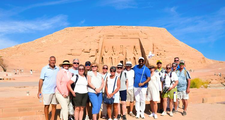 Eine Reisegruppe posiert vor der monumentalen Fassade des Abu Simbel Tempels unter einem leuchtend blauen Himmel.