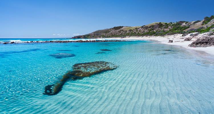 Kristallklare türkisblaue Bucht mit versunkenen Schiffswrackresten und weißem Sandstrand.
