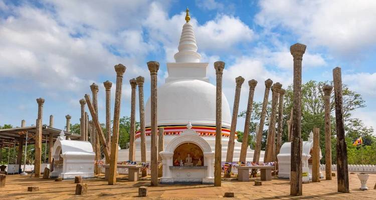 Witte stupa omringd door hoge stenen zuilen onder een gedeeltelijk bewolkte hemel bij Mihintale.